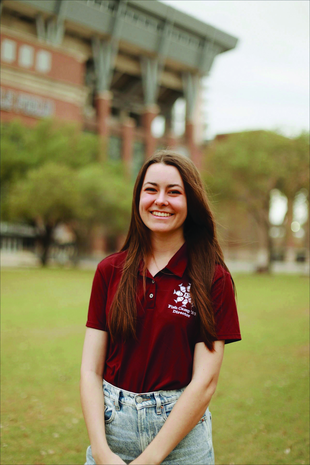 A headshot of a young woman smiling while wearing a maroon Fish Camp polo and standing in front of Kyle Field.