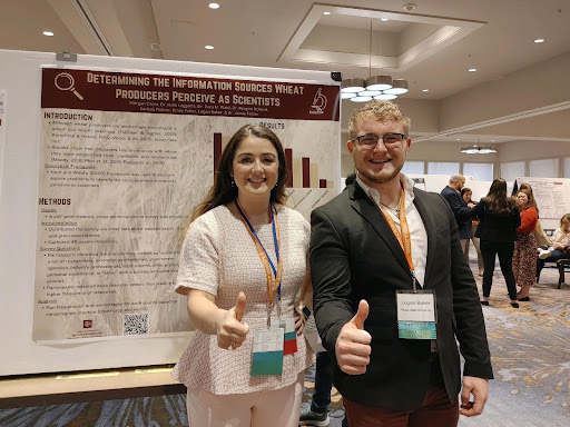 Two people posing with a thumbs up and standing in front of a research poster.