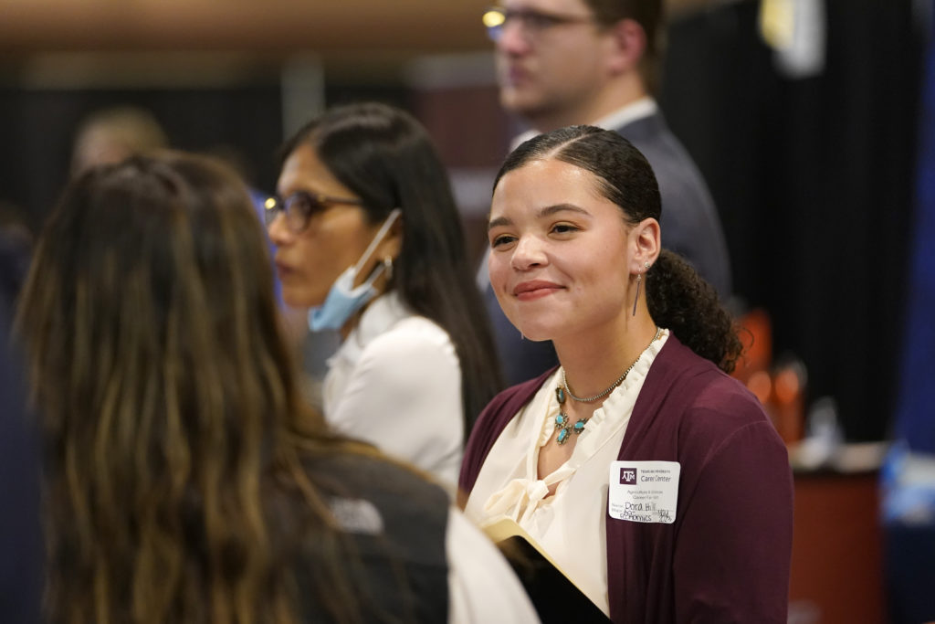 Woman smiling at another woman in the crowd of a busy career fair