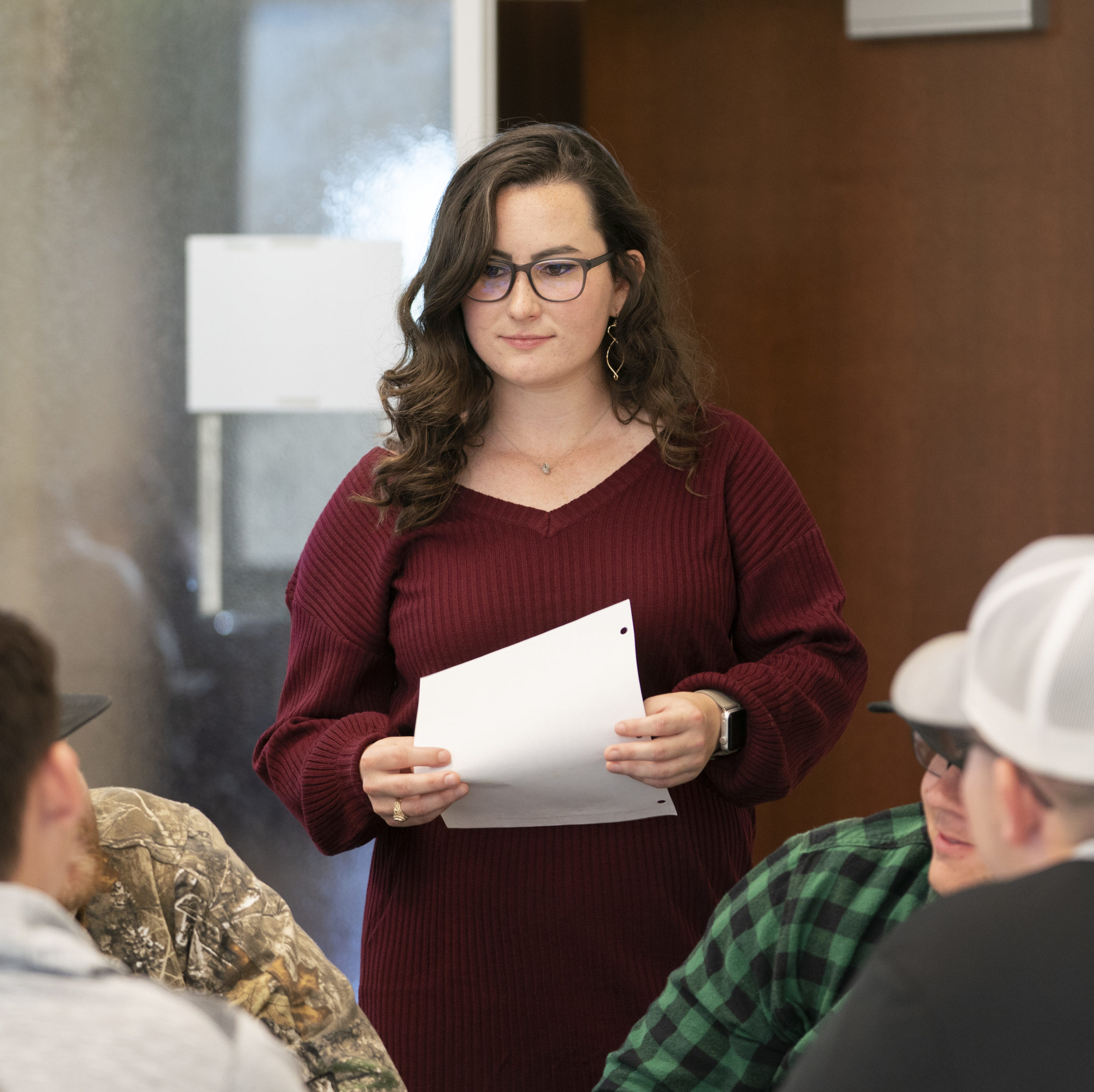 Woman holding a piece of paper stands above a group of students