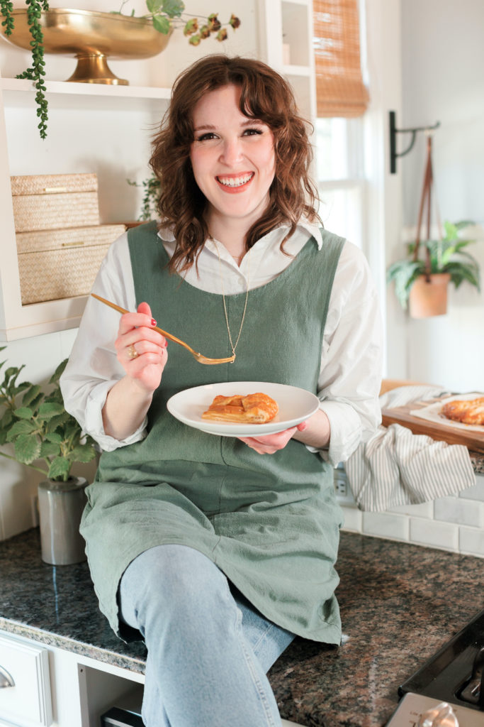 Heather Janak holding a dessert in her hand with a fork in another sitting in a living room