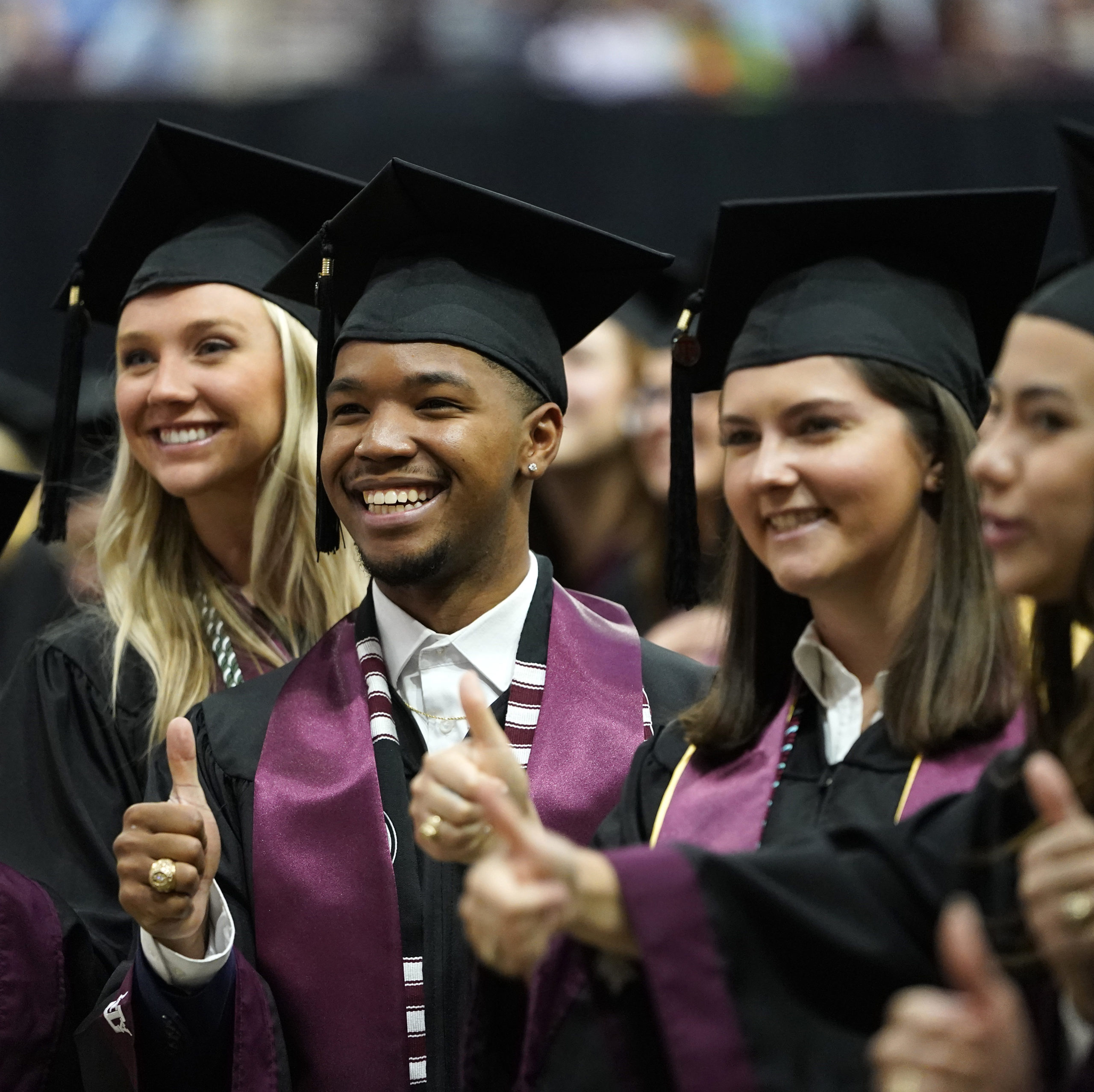 Aggies wearing graduation gowns posing with Gig 'Em thumbs